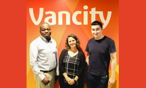A woman and two men stand in front of the Vancity logo