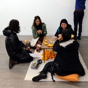 The Body Envelope workshop participants sitting on the floor around a small table, peeling oranges.