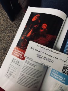 A PuSh Festival guide open to the page about Old Stock: A Refugee Love Story with a ticket to the show resting on top of the page.