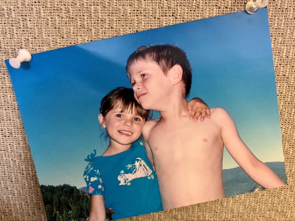 A brother and sister pose smiling at the beach.