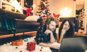 In a festive living room, a couple looks a laptop screen.