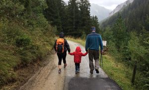 Two adults and a child walk down a trail on a rainy day while holding hands