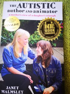Picture of a book called "The Autistic Author and Animator: A Mother's View of a Daughter's Triumph. On the cover of the book, two women are sitting on a concrete staircase outdoors. The one on the left is blonde and is wearing a blue button-up shirt, while the one on the right is brunette and is wearing a denim jacket.