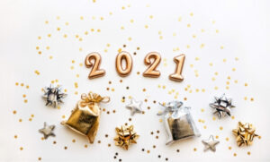 "2021" is spelled out in gold numbers. It is surrounded by gold star confetti and small silver and gold presents with bows.